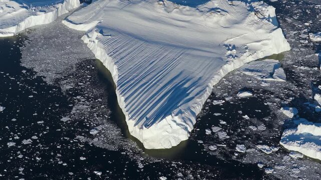 Aerial view of massive iceberg from Ilulissat glacier floating in dark arctic waters surrounded by scattered ice fragments in Greenland.