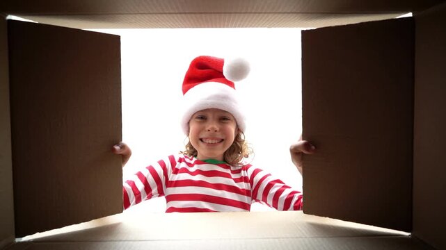 Happy child is unpacking a Christmas gift box. Girl dressed in Xmas pajamas is having fun at home. Slow motion