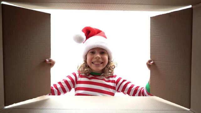 Happy child is unpacking a Christmas gift box. Girl dressed in Xmas pajamas is having fun at home. Slow motion