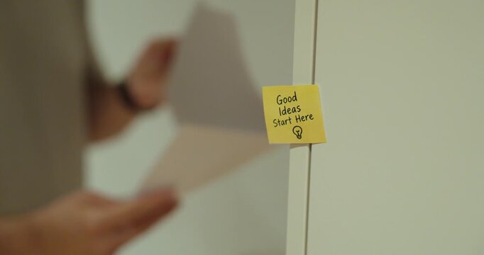 Motivational sticky note saying Good Ideas Start Here with a person working in the background.