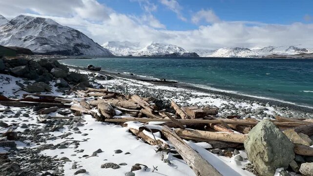 Cinematic steady shot of bright turquoise waves hitting a pebbled, snow-covered beach in winter.
