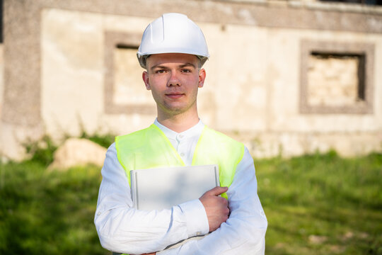 Architectural consultant wearing hard hat and safety vest holding laptop at renovation site. Construction business architectural consultancy and project planning
