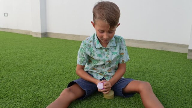 Boy Sitting on Artificial Grass Playing With a Pink Toy