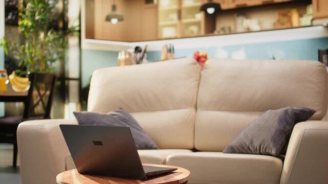 Living room interior with laptop on round coffee table, warm tones and natural light in an empty rustic home. Wooden table and couch create a modern atmosphere with no people indoors.