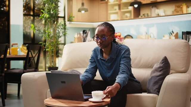 Female digital nomad uses laptop at kitchen table, enjoying relaxed freelancer lifestyle and flexible work while telecommuting indoors for productivity.
