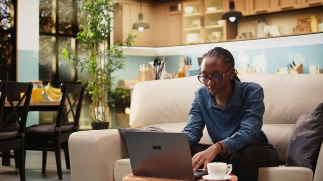 Smiling woman works from home in cozy rustic living room, using laptop for daily online tasks with remote work setup supporting productivity at home.