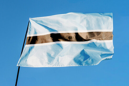 Flag of Botswana. Flag waving in the wind against a clear blue sky, fluttering on a flagpole outdoors. Bright sunny day, fabric texture, outdoor close-up view