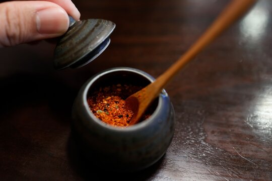 七味唐辛子が入った小さな陶器の薬味入れ。木製さじ付き