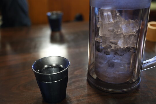 氷入りのお冷のピッチャーとコップ。飲食店の木製テーブル
