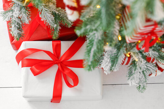 Beautiful presents, gift boxes wrapped in elegant red paper under green snowy festive Christmas tree with warm lights. Cozy winter holiday atmosphere perfect for seasonal celebrations and decor themes