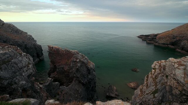Natural rock formations frame a sheltered coastal inlet with calm green seawater and a distant horizon.