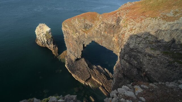 A large natural rock arch extends above dark seawater beside a rugged limestone headland on the Pembrokeshire coast.