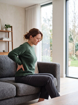Woman sitting on couch suffering from lower back pain at home