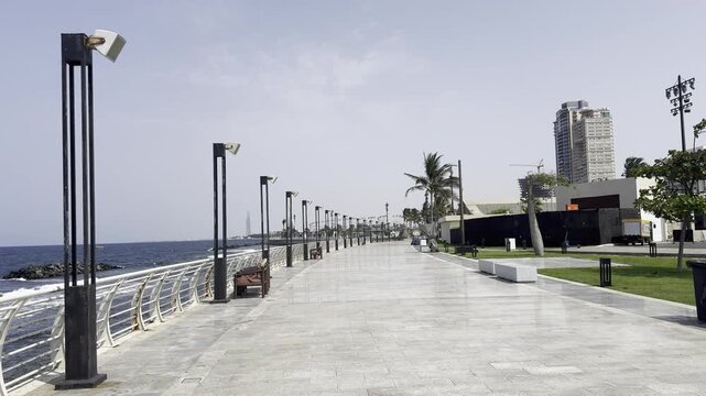 Modern paved pedestrian promenade along Jeddah Corniche waterfront with street lamps, palm trees, and Red Sea coast, Saudi Arabia