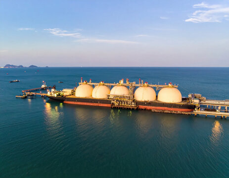 Aerial view of liquefied gas carrier at industrial marine terminal beside calm blue ocean under clear sky