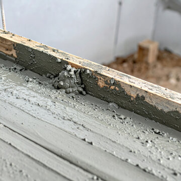 Cement mortar on wooden formwork creates rough gray construction surface with scattered aggregate and unfinished texture