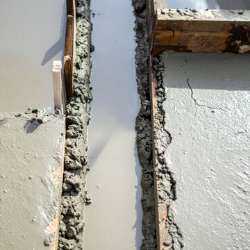 Construction joint between concrete wall and plaster surface with wooden formwork, rough texture, and repair detail