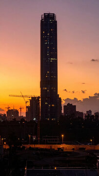 Skyscraper construction silhouette against glowing sunset city skyline with tower crane and urban building detail