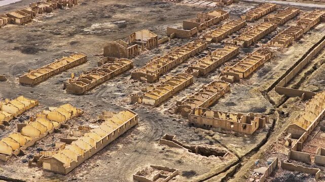 High angle perspective shows ruined mud brick buildings in an abandoned desert town under bright daylight, highlighting desolate architecture.