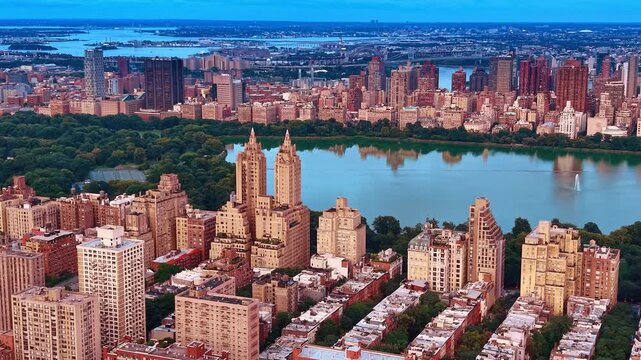 Lush green Central Park surrounded by reddish-brown architecture. Sprawling panorama of New York City, USA in the backdrop.