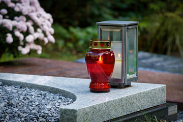 Modern curved marble gravestone with red burning candle, lantern, and white gravel bed in a serene cemetery. © gehapromo