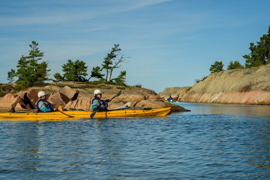 Two paddlers in a yellow tandem kayak glide through a narrow granite channel as the group paddles ahead with copy space on Georgian Bay, Ontario, Canada