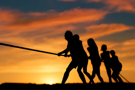 Silhouette of a team pulling on a rope against a vibrant sunset sky
