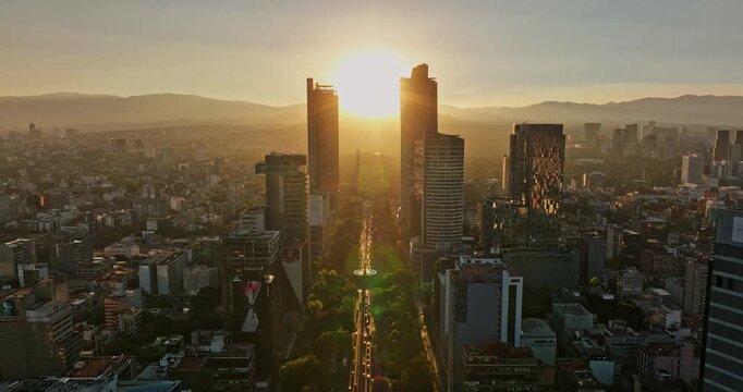 Mexico City Aerial v24 reverse flyover capturing dramatic glowing sun shinning on paseo de la reforma in between high rise buildings at sunset golden hours - Shot with Mavic 3 Cine - December 2021