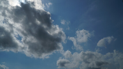 Obraz premium Dramatic Sun Peeking Above Dark Cloud in Blue Sky with Scattered Clouds