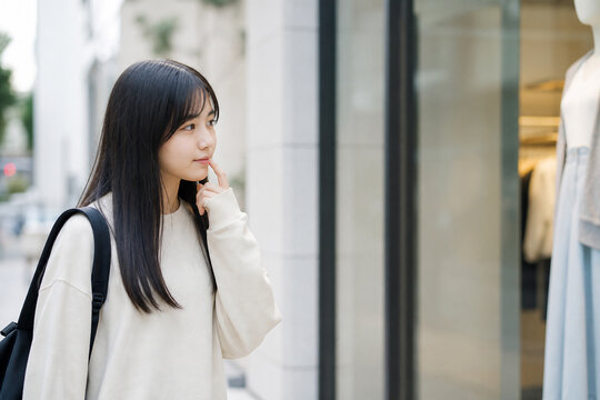 店舗のショーウィンドウを見て考える若い女性