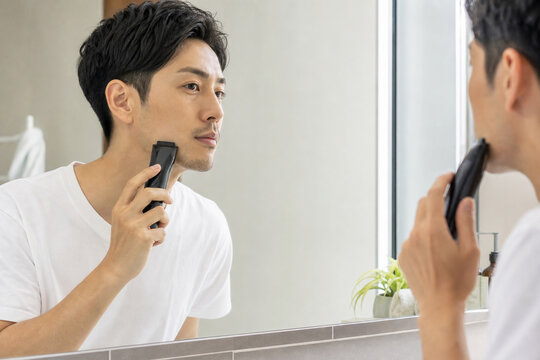 鏡を見ながら電気シェーバーでひげを整える男性