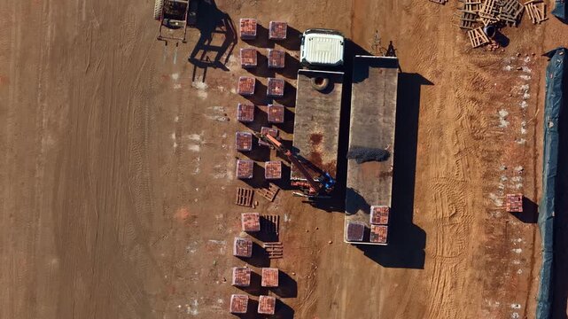 Worker uses truck-mounted crane to load clay brick pallets on a flatbed trailer