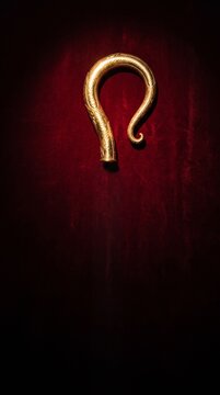 Golden crosier staff crook headpiece illuminated on deep red velvet background, Saint Nicholas Day and Sinterklaas religious tradition concept