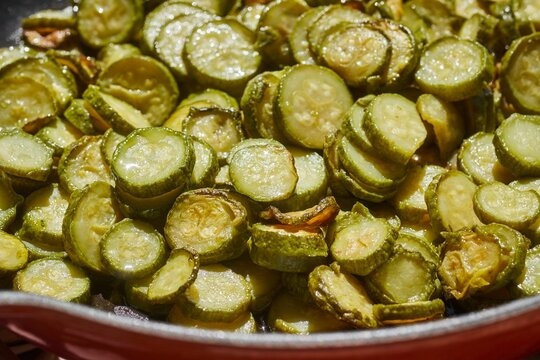 Slices of zucchini frying in a skillet. In some places, they're called courgettes.