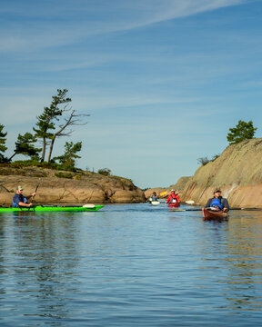 Vertical view of sea kayakers paddling toward camera through a granite channel in morning light with copy space on Georgian Bay, Ontario, Canada