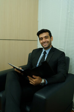 An executive is sitting on the sofa, holding a document folder and preparing for a meeting.