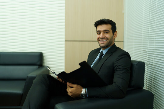 An executive is sitting on the sofa, holding a document folder and preparing for a meeting.