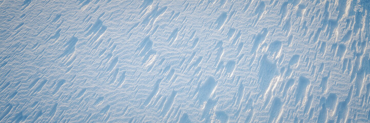 Beautiful winter background with snowy ground. Natural snow texture. Wind sculpted patterns on snow surface. Wide panoramic texture for background and design. © Andrei Stepanov
