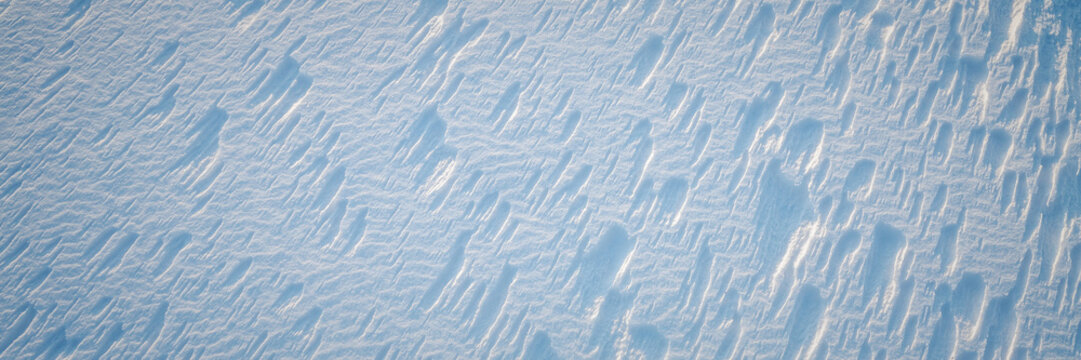 Beautiful winter background with snowy ground. Natural snow texture. Wind sculpted patterns on snow surface. Wide panoramic texture for background and design.