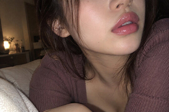 暗い室内で光沢のある唇を見せる紫のニット姿の女性の接写