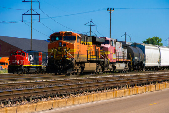 Granite City, IL, July 27, 2018 &mdash; BNSF and Canadian National freight locomotives stand beside rail cars in a rail yard, illustrating competing North American freight networks.