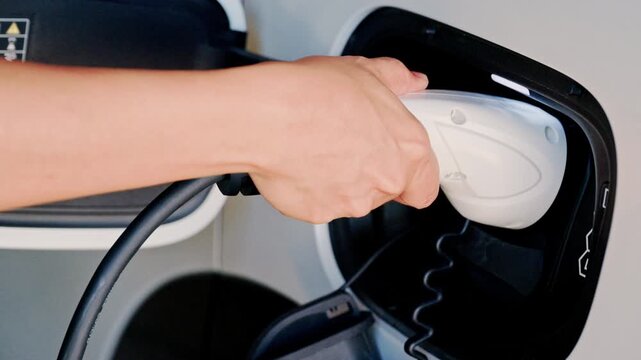 4K Person plugging in EV charging cable to white electric vehicle for sustainable energy transport