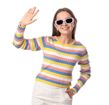 Friendly greeting and positive communication, young woman waving hand with smile wearing colorful striped sweater and sunglasses isolated on white background