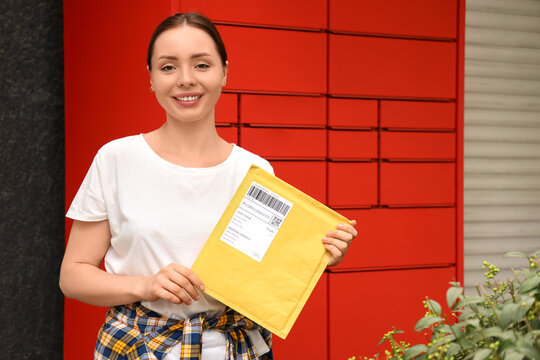 E-commerce delivery and online shopping, happy woman holding a yellow padded envelope in front of a red parcel locker for package pickup and shipping