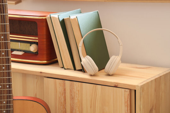 Hobbies and leisure time, wireless headphones with books and vintage radio on wooden shelf for music listening and reading relaxation at home