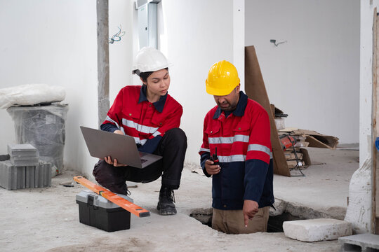 Construction engineer reviewing project information on a laptop while coordinating with a technician inspecting underground utilities during building renovation. Site safety, quality control, teamwork