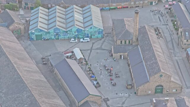 Elsecar Heritage Centre New Yard workshops with historic stone ranges, industrial courtyard, chimney and sawtooth roof, South Yorkshire, England, drone descent