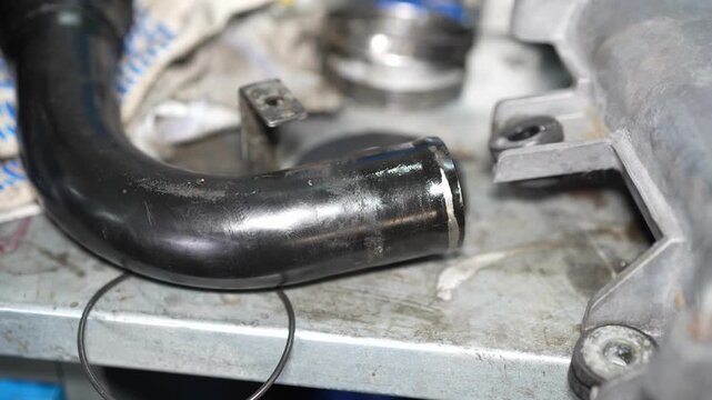 A close-up shot of a disconnected black plastic or rubber automotive pipe with an O-ring groove, lying on a metal workbench during repairs.