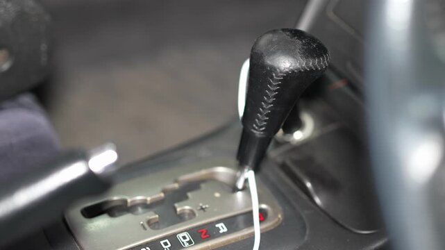 A close-up shot of a car's center console, featuring an automatic transmission gear selector lever with chrome accents and a wood grain trim panel.