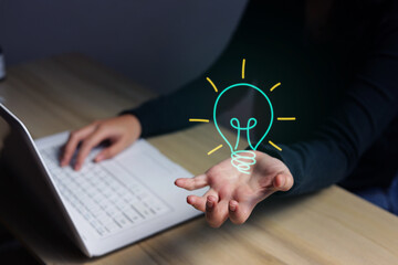 Woman Typing on Laptop while Presenting Illuminated Light Bulb Graphic © Queenmoonlite Studio